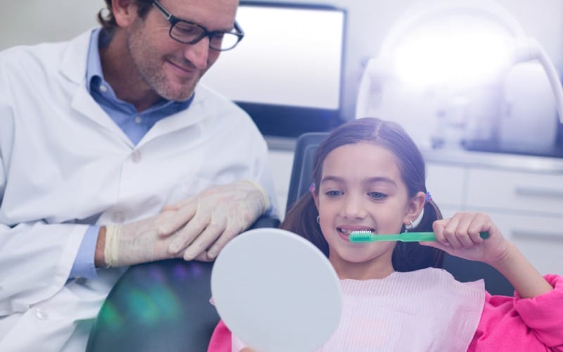 dentist assisting young patient while brush teeth