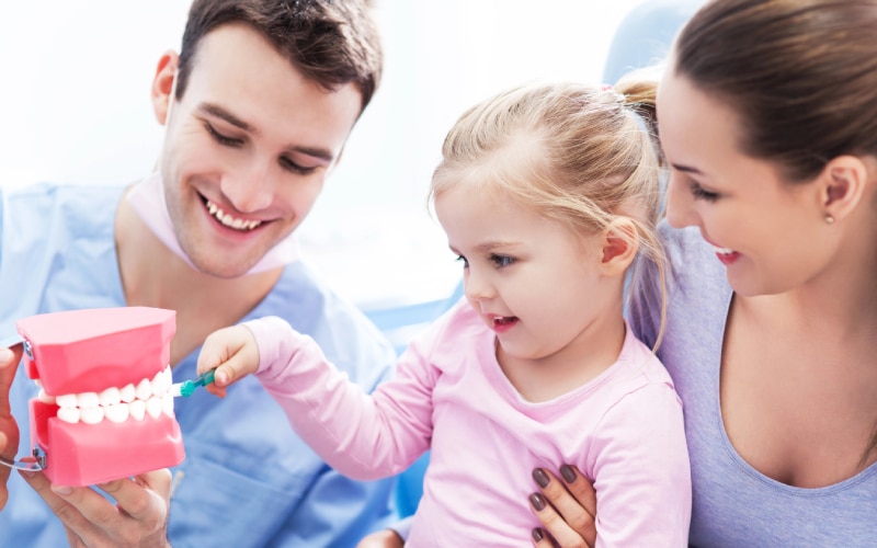 dentist teaching girl how-to brush teeth