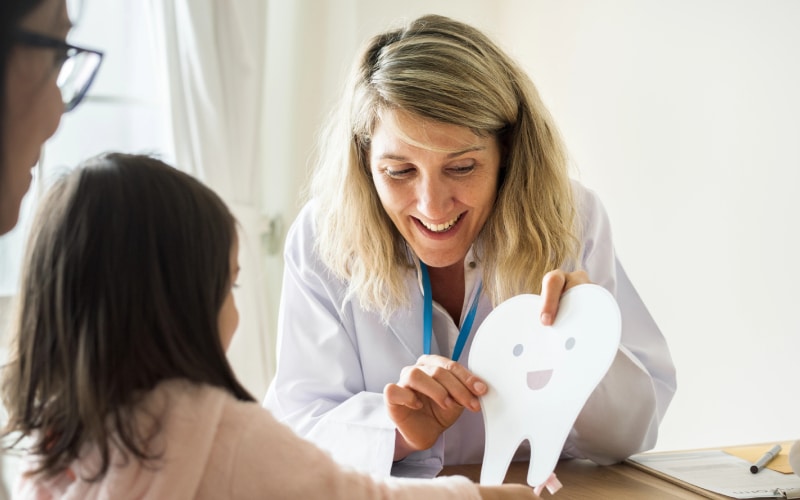 dentist teaching little girl how brush teeth